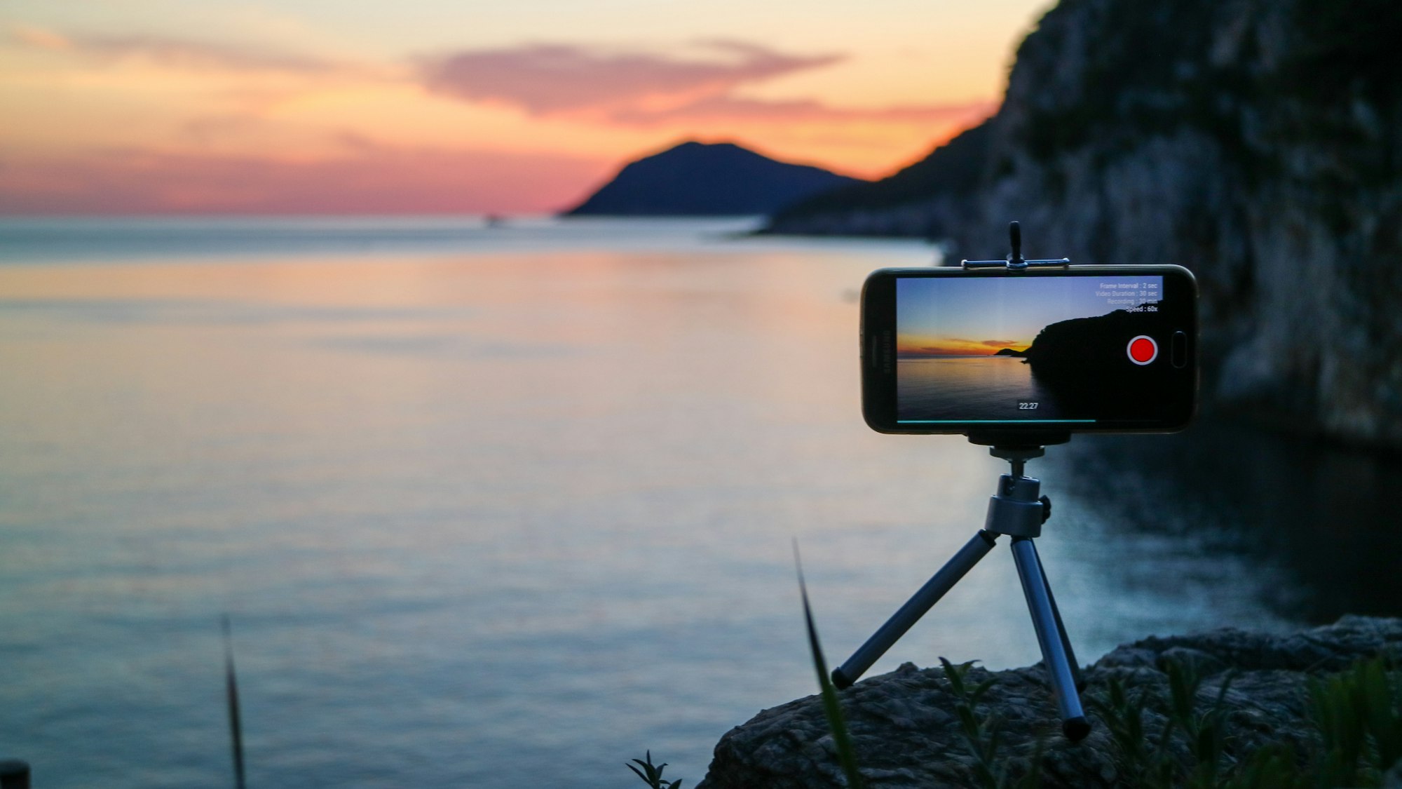 A phone on a mini tripod filming the coastline at sunset